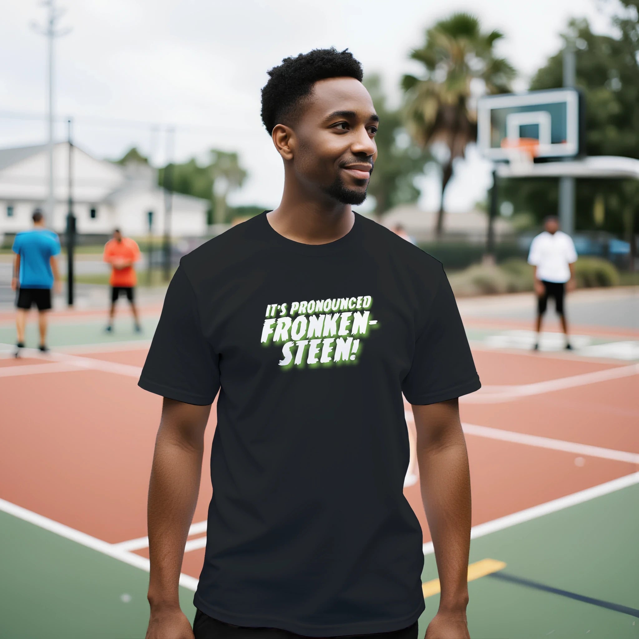 Man wearing a black t-shirt with 'IT'S PRONOUNCED FRONKEN-STEEN' text on a basketball court.