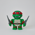 Toy figure of a green turtle with red bandana and grey sais on a light beige surface and backdrop