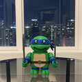 Toy turtle with blue shell holding swords in front of a window with city skyline view